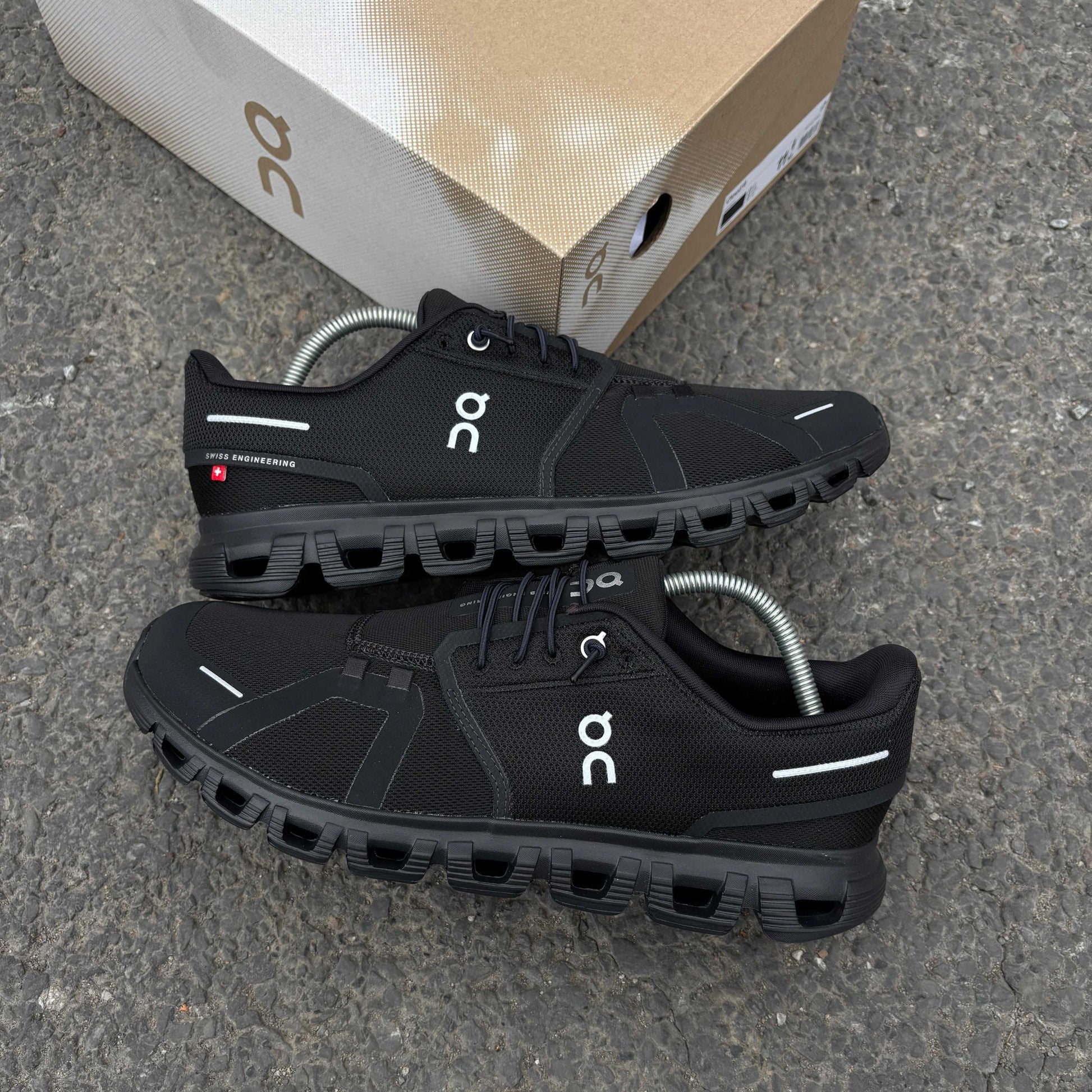Black athletic shoes with 'on' branding on a gray surface, with a cardboard box in the background.
