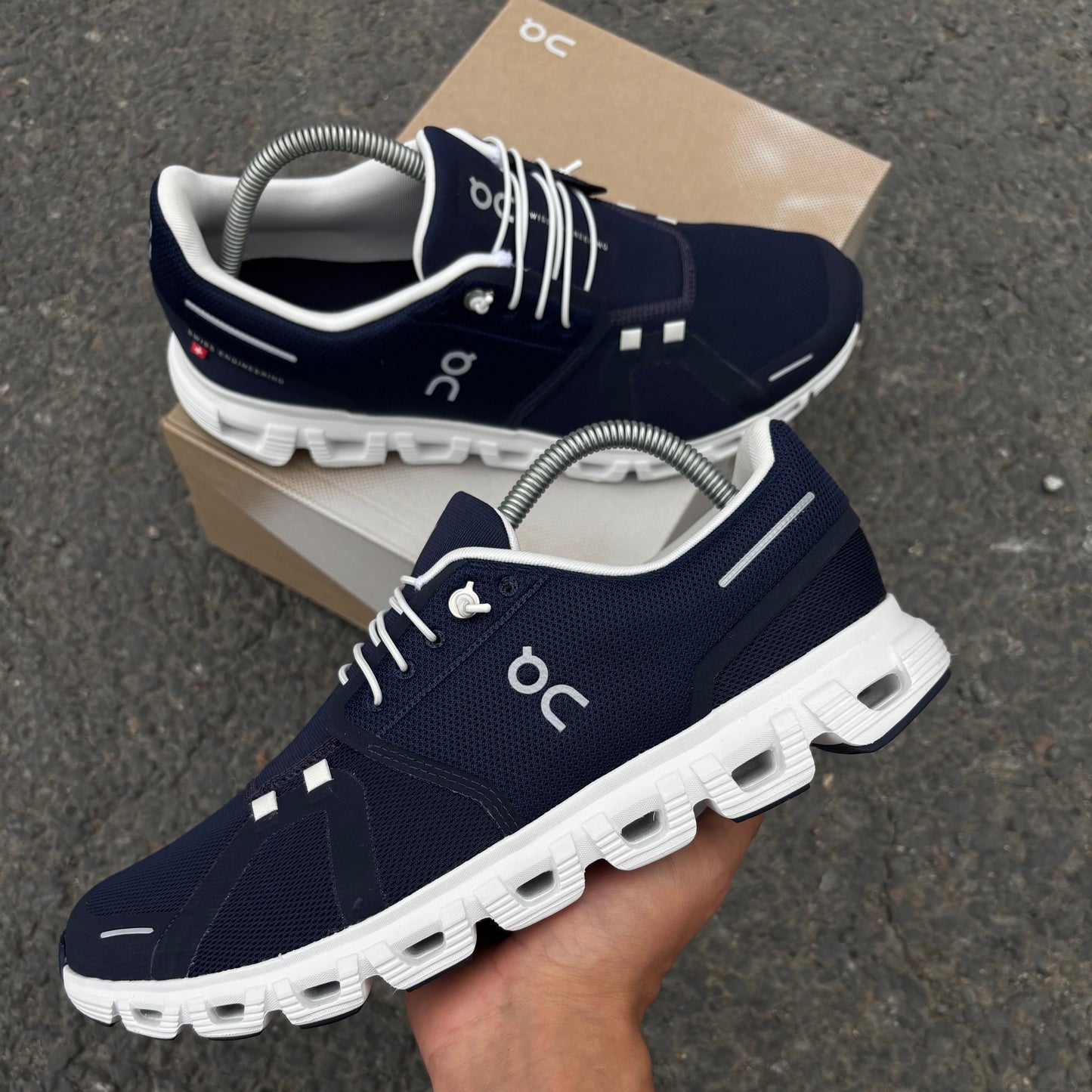 Navy running shoes with white soles held by a hand on a dark surface