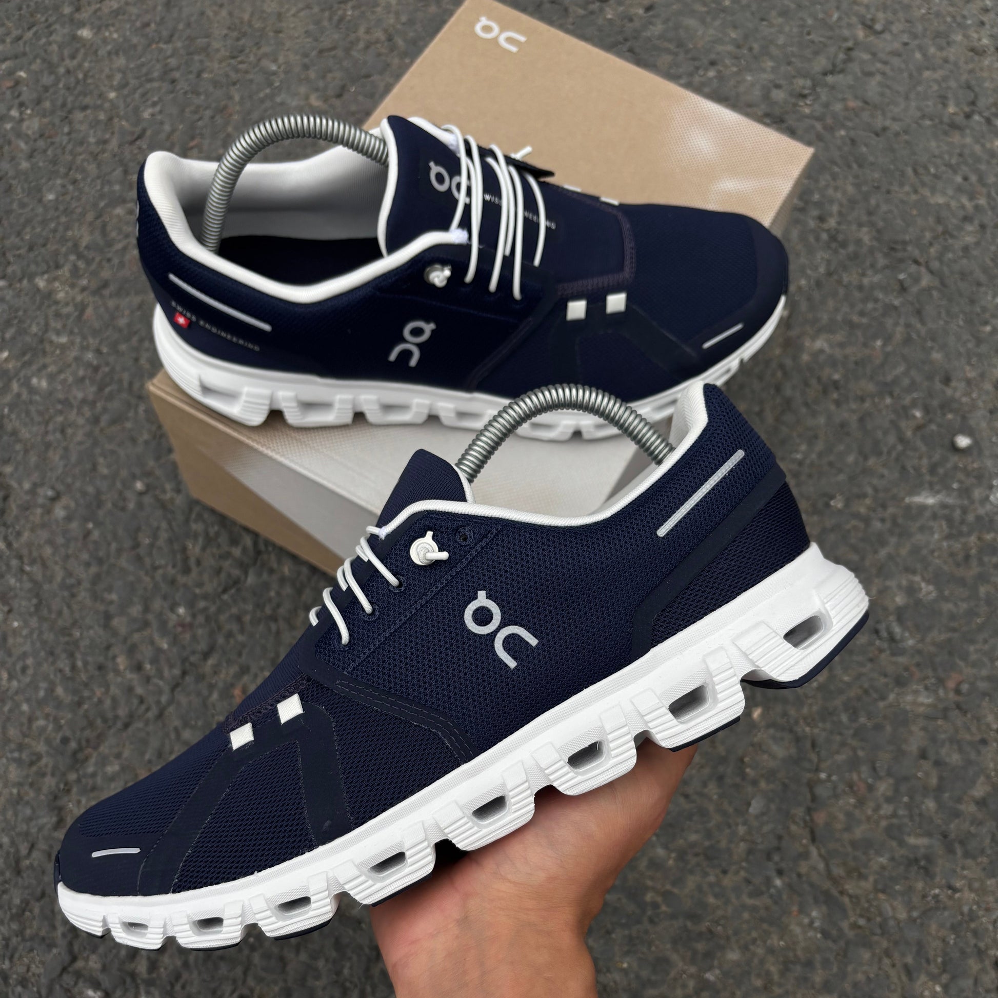 Navy running shoes with white soles held by a hand on a dark surface