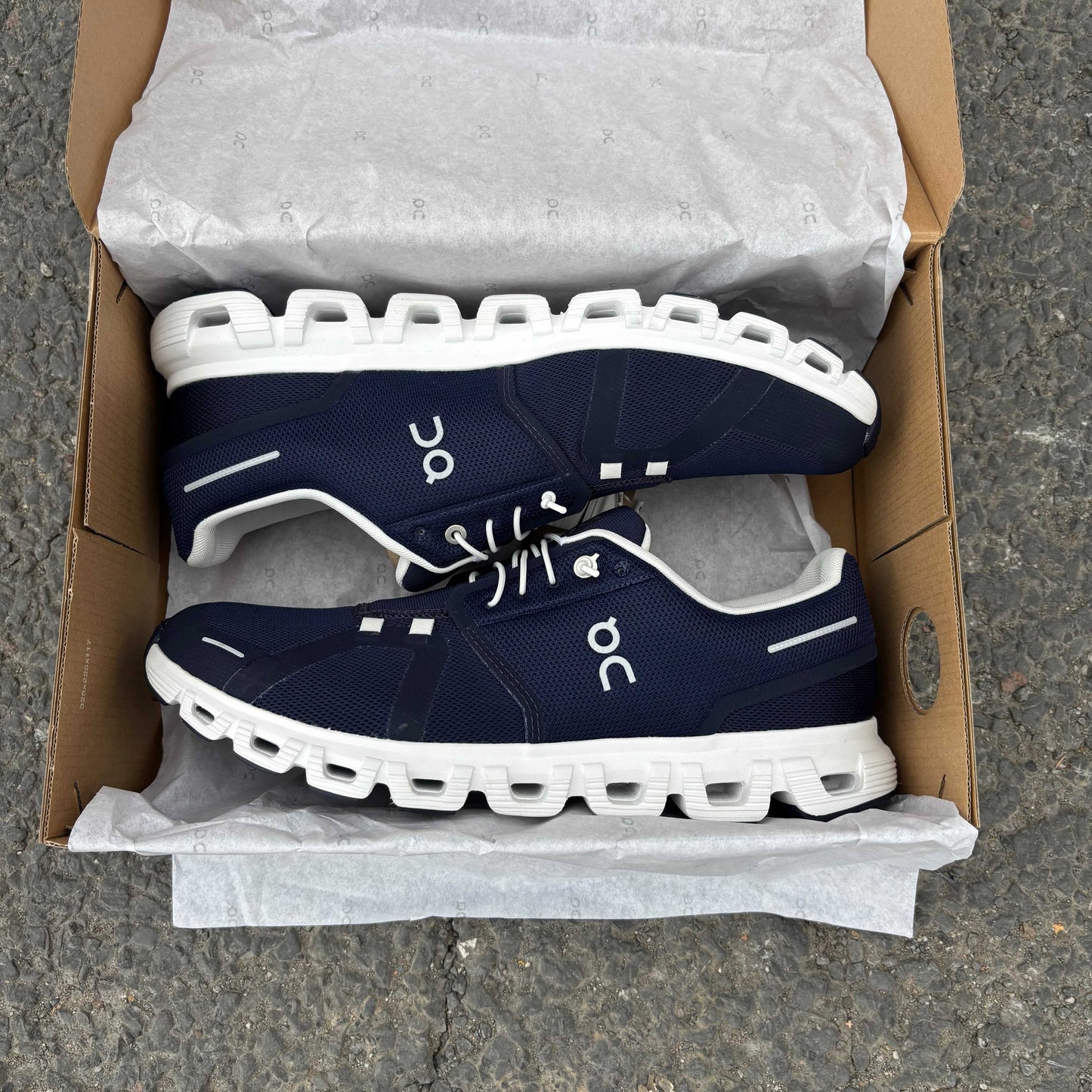 Navy and white sneakers in an open cardboard box on a concrete surface